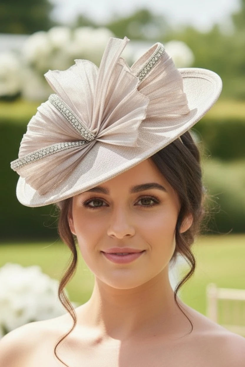 Woman wearing a large champagne fascinator hat with a bow and embellishments outdoors.