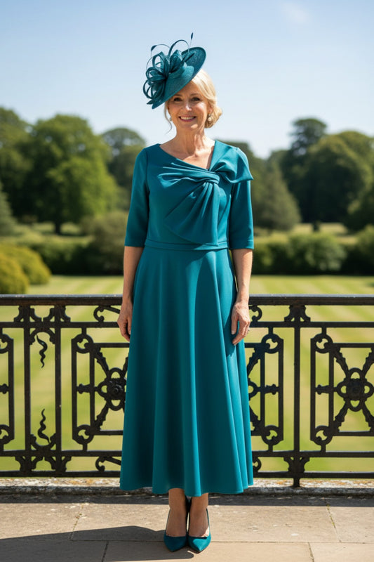Ispirato ISL805 green Mother of the Bride dress with flowing skirt, defined waistline and statement bow, shown outdoors in natural light