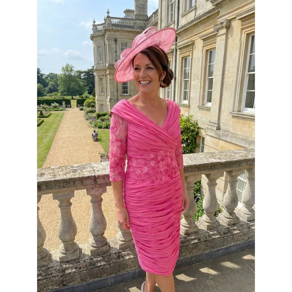 Ispirato ISJ823 pink mother of the bride dress with ruched bodice and embellished lace sleeves, shown outdoors at a stately venue.