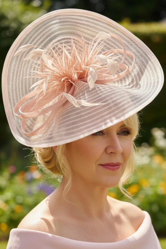 Woman wearing a large blush decorative pink fascinator hat with floral details against a blurred natural background.