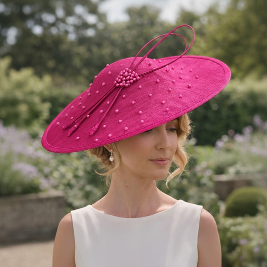 Woman wearing a jbees fushia pink fascinator hat with a white dress in a garden setting
