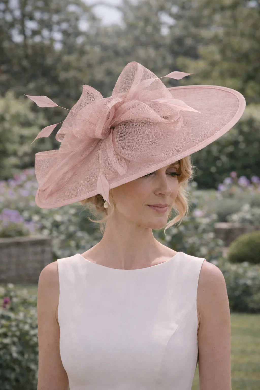 Woman wearing a jbees large pink fascinator hat with a bow outdoors