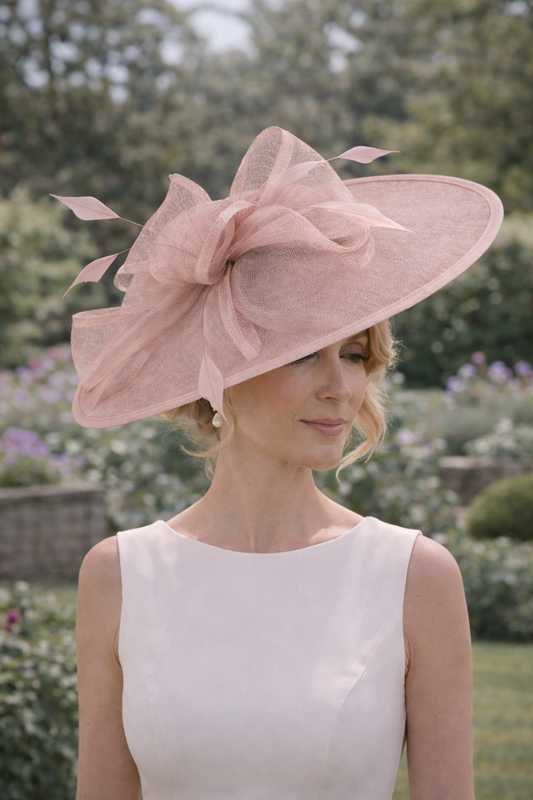 Woman wearing a jbees large pink fascinator hat with a bow outdoors