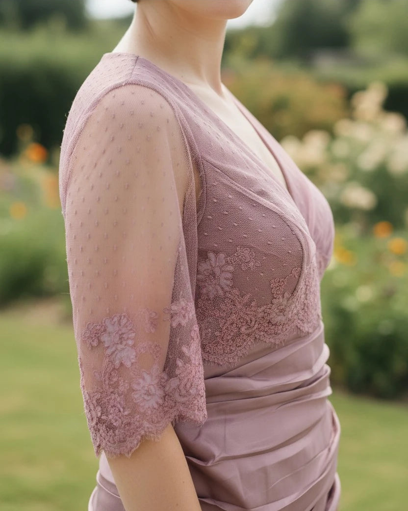 Woman wearing a light pink mother of the bride lace dress with sheer sleeves in a garden setting