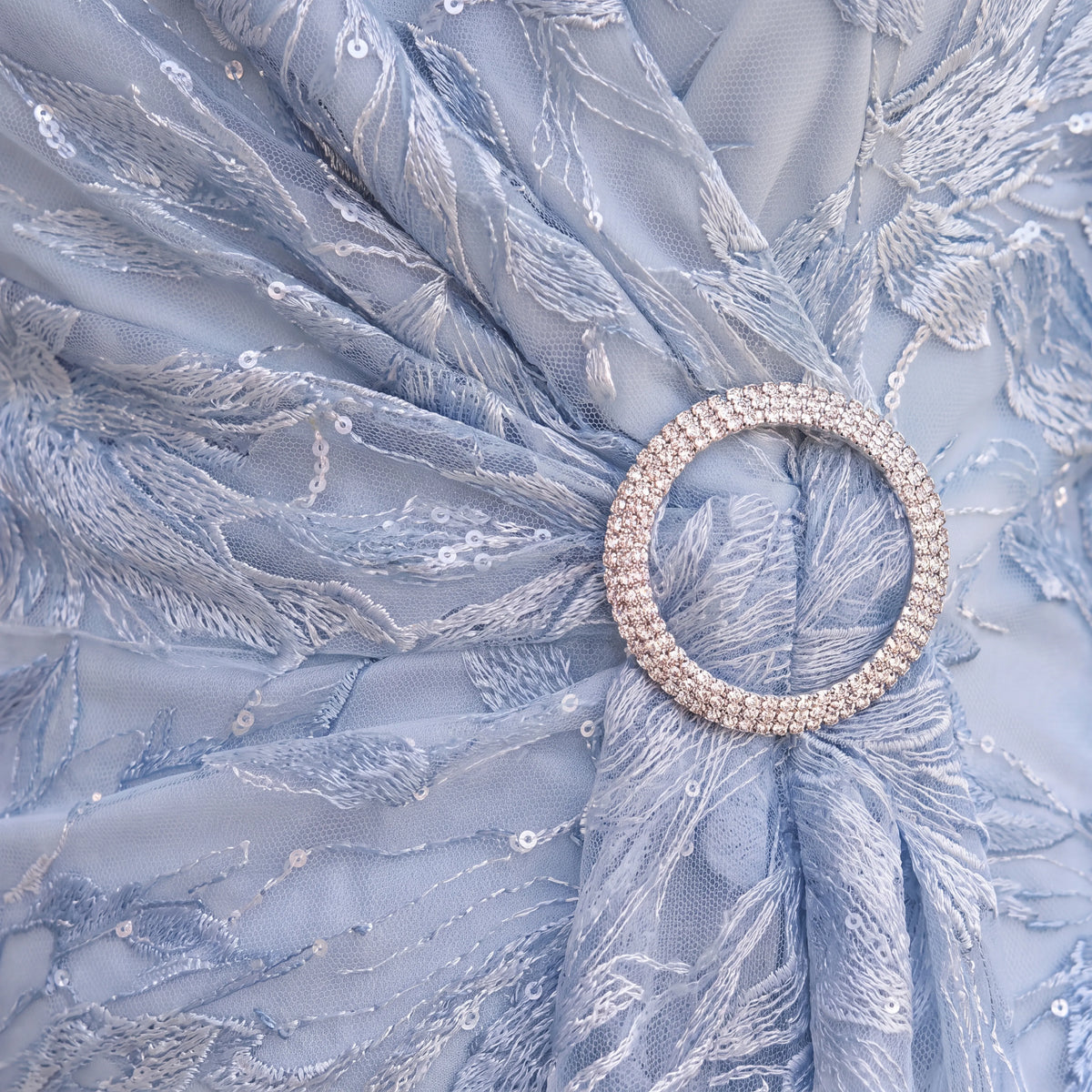 Detail of the light blue Ispirato ISH814 Mother of the Bride dress showing the embellished circular waist buckle and intricate lace fabric.