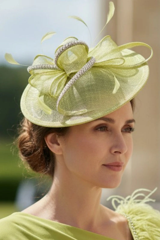 Woman wearing a light lime green decorative fascinator hat with a large bow, and embellishments outdoors.