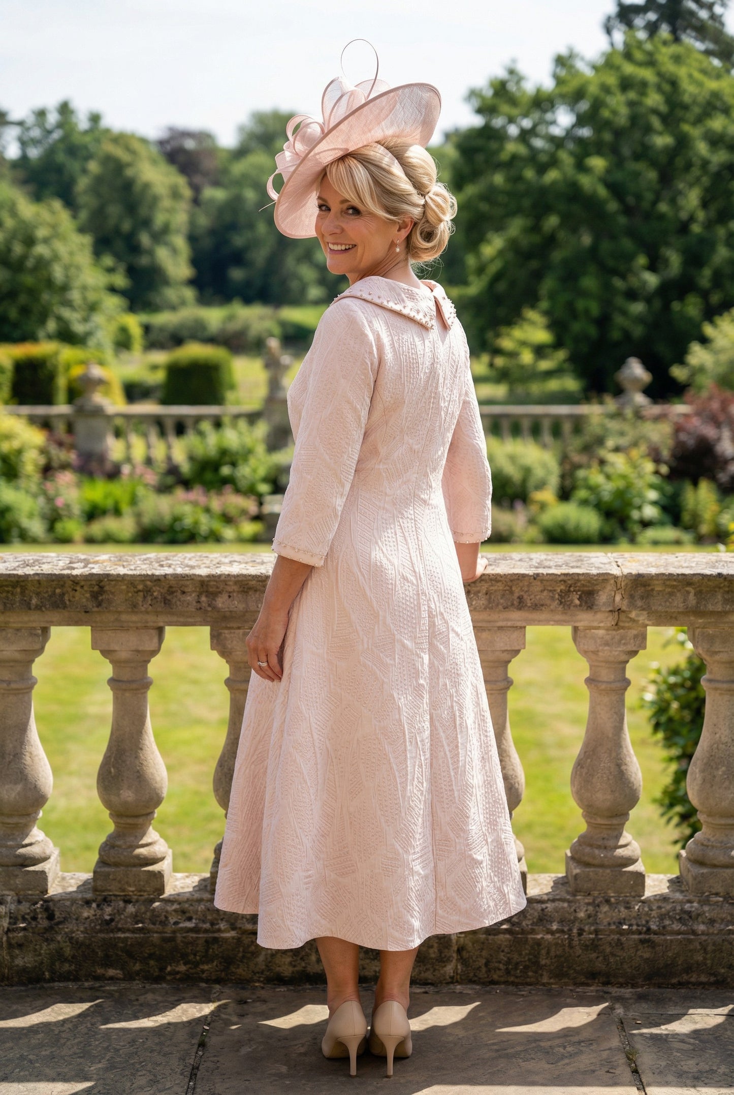 Back view of a woman wearing a lizabella light pink mother of the bride dress dress in an outdoor setting