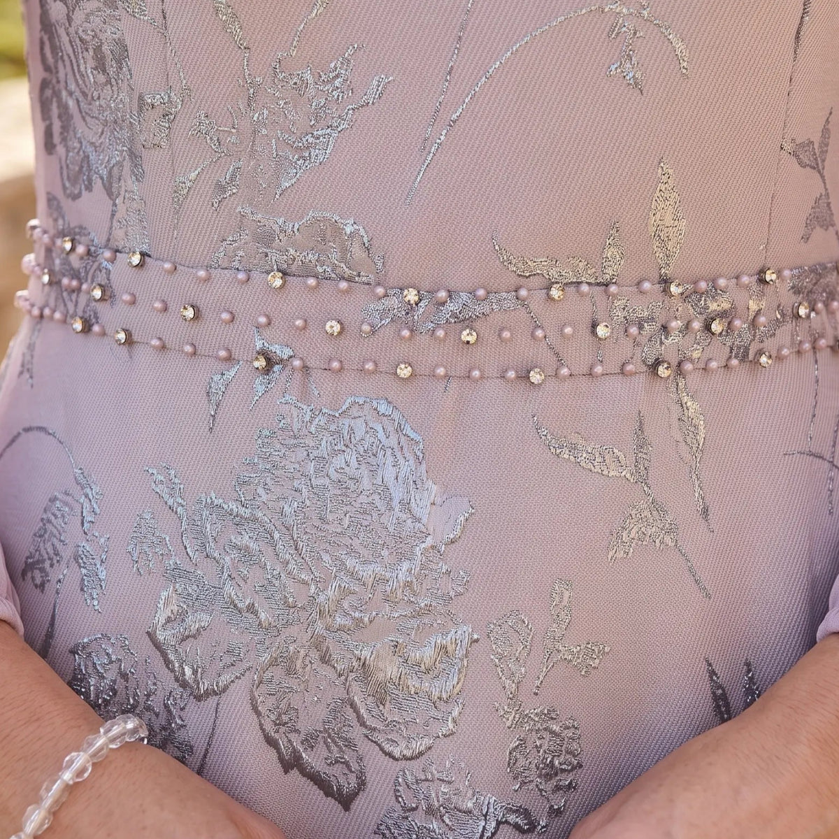 Close-up of the metallic floral jacquard fabric and pearl embellished waistband on the Lizabella 2809 lilac mother of the bride dress.