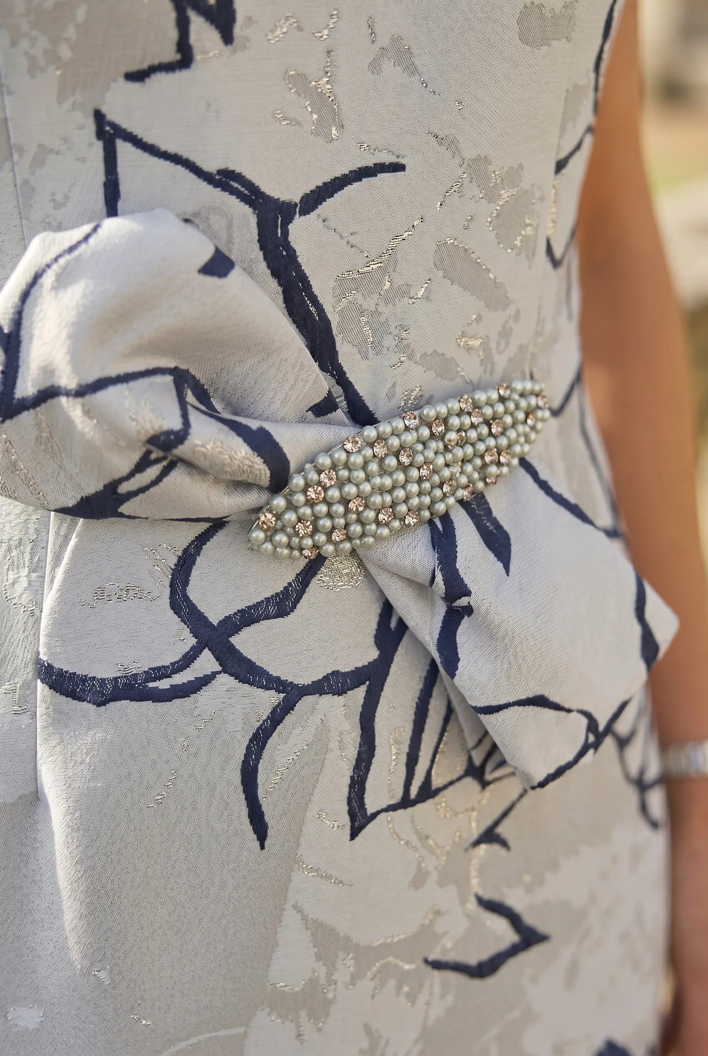 Close-up of a 2 piece mother of the bride outfit with a decorative bow and floral pattern. Signature Dress