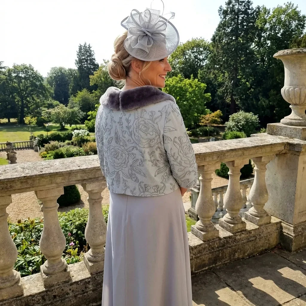 Lizabella Dress 7168 styled with a wide‑brim hat, showing full silver and ice‑blue outfit in an outdoor setting.
