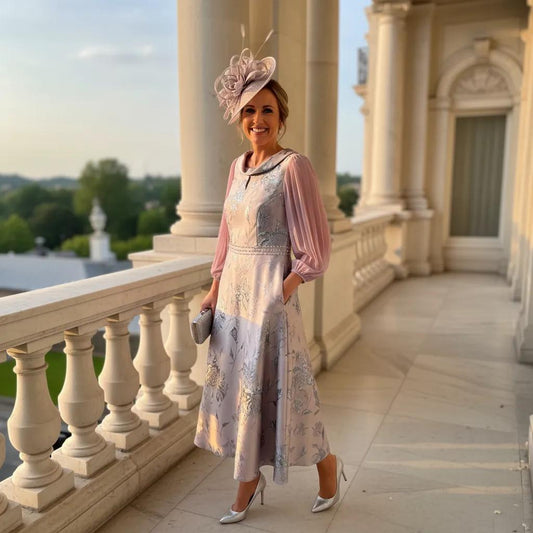 Woman in formal lilac mother of the bride dress and matching embellished fascinator hat standing on a balcony with classical architecture.
