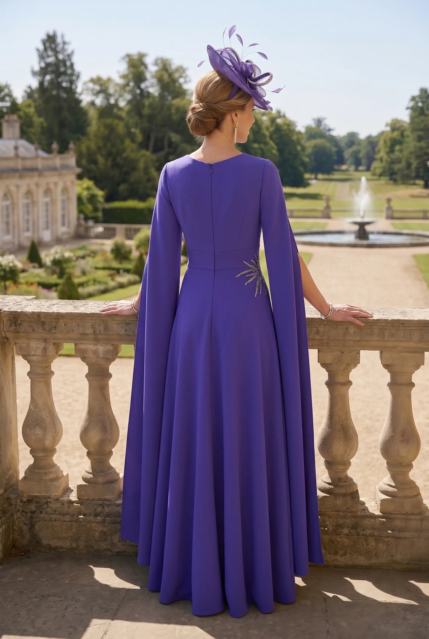 Woman in a purple mother of the groom dress standing on a balcony with a garden and fountain in the background