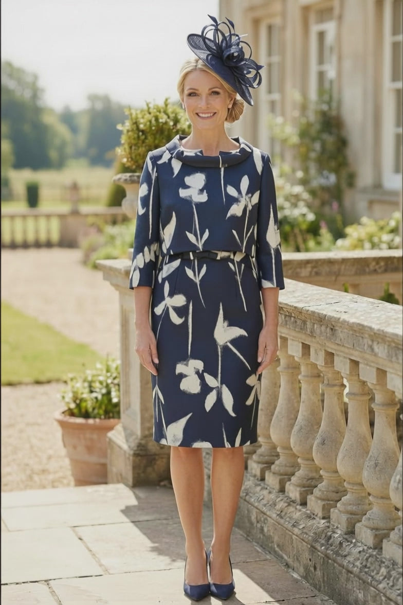 A video of a Navy floral mother of the bride dress with matching navy fascinator, walking on a stone terrace overlooking a formal garden.