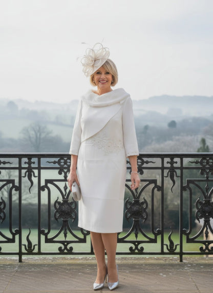 Woman in a white fur bridal dress with a matching hat standing on a balcony with a scenic background.