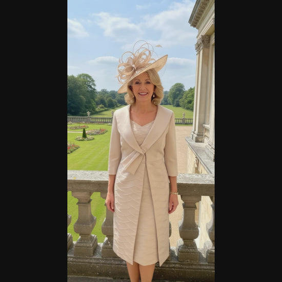 Woman in a beige lizabella 2662 mother of the bride outfit standing on a balcony with a garden view at a wedding - signature dress