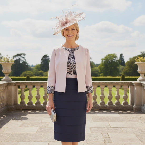 The Condici dress and jacket set in grey and blush pink boasts a flattering layered skirt. The ensemble features a lace bodice with elbow-length sleeves and is complemented by a contrasting jacket adorned with lace cuffs.