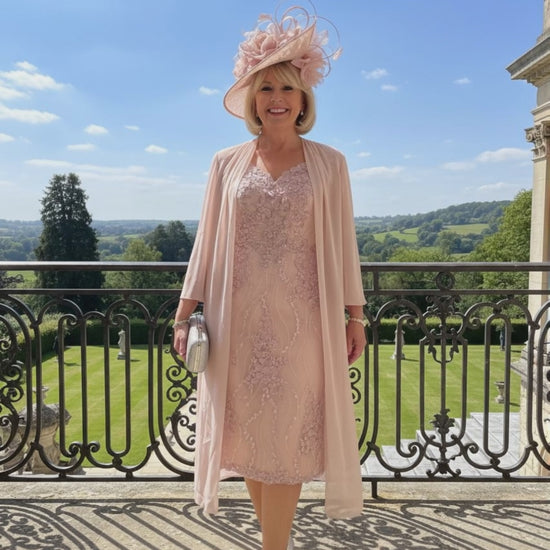 Woman in a light pink veni infantino 991447 v neck dress and hat standing on a stone balcony