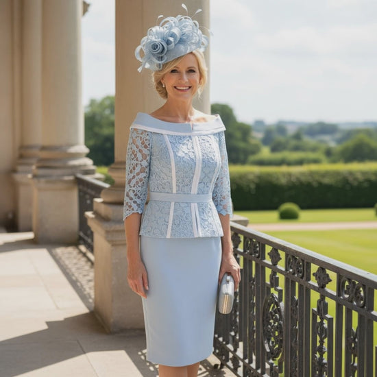 Woman in a veni infantino light blue lace mother of the bride dress and light blue fascinator standing on a balcony with a garden view. Signature Dress.