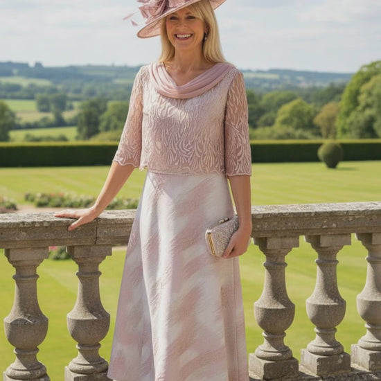 Woman in a pink Lizabella Mother of the bride dress and hat standing on a stone balcony with a scenic background
