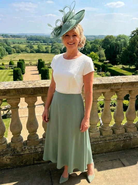 Richard Designs RDAD1159 sage mother of the bride outfit with ivory pearl top, sage skirt and matching hat on a garden terrace.