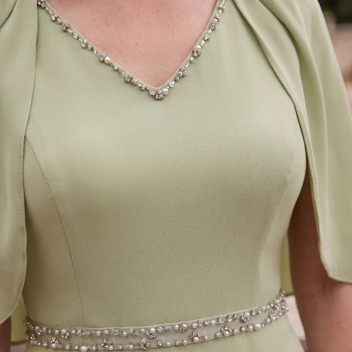 Close-up of the Couture Club 7G178 Sage Green Mother of the Bride dress showing the crystal V-neckline, waistband and cape detailing.