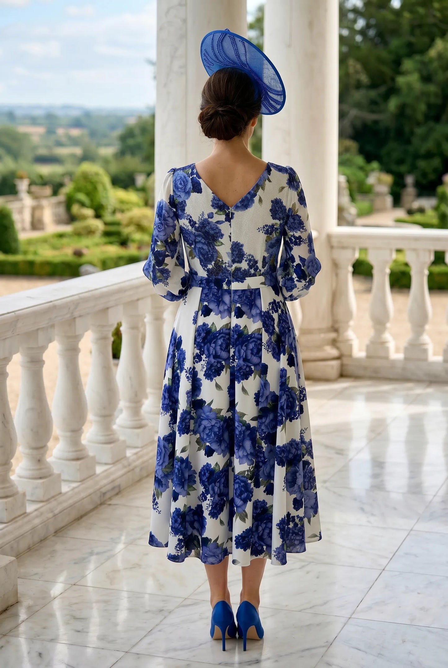 Woman in a blue floral dress standing on a balcony with a scenic view.
