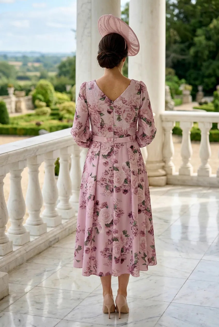 Woman in a veromia pink floral mother of the bride dress standing on a balcony with a scenic view.