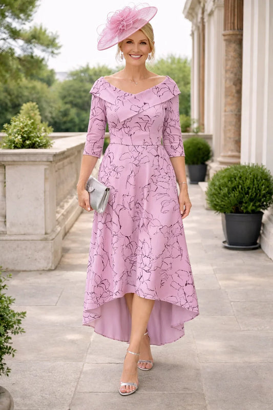 Woman in a Veromia pink high low dress with a matching pink fascinator hat standing outdoors.